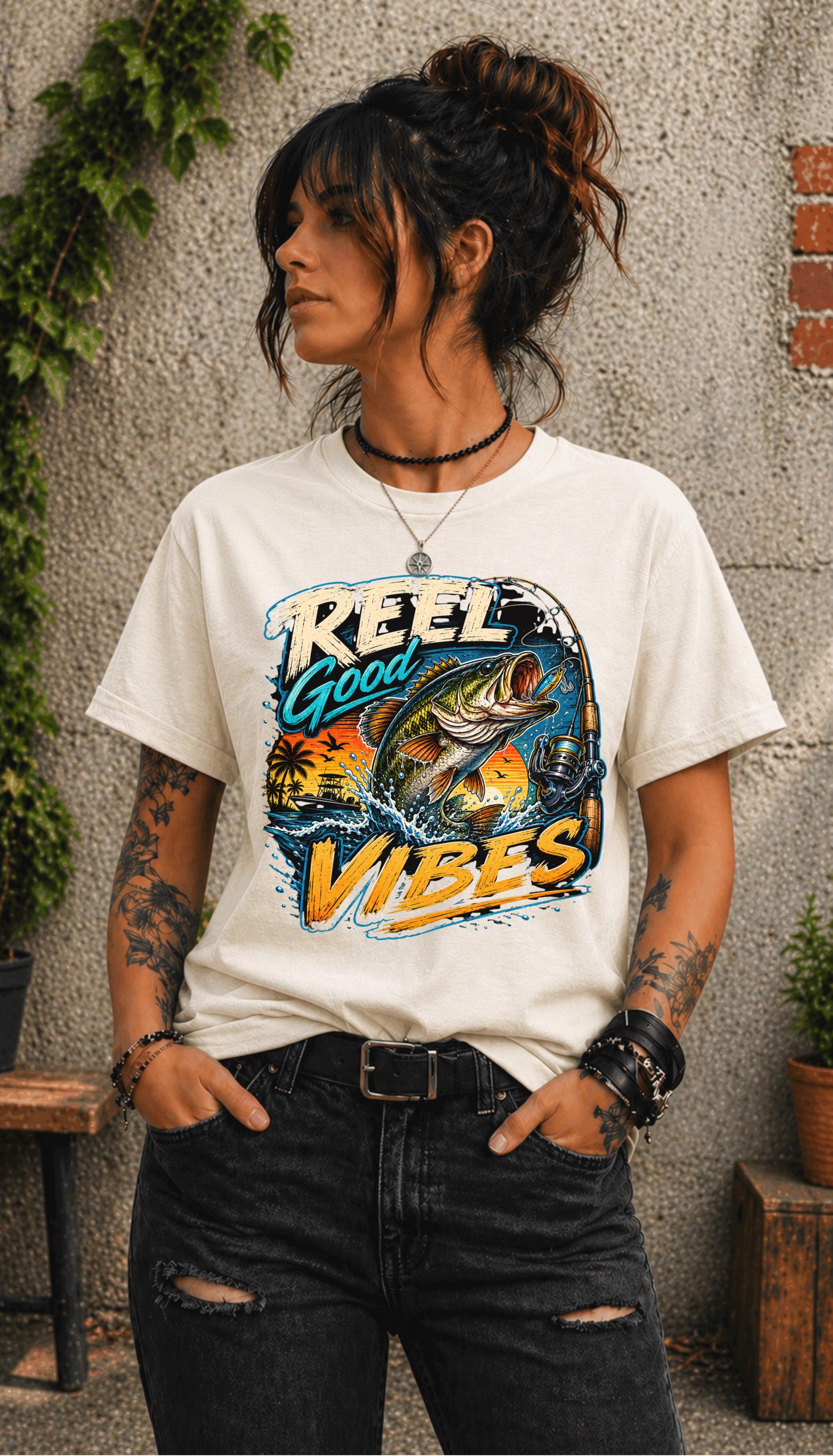 Woman wearing a graphic t-shirt featuring a jumping bass fish, fishing rod, tropical sunset scene, and Reel Good Vibes lettering.