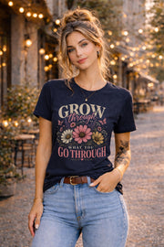 Woman wearing a floral inspirational t-shirt featuring the quote "Grow Through What You Go Through" with pink and cream flowers and butterflies in a soft vintage design.