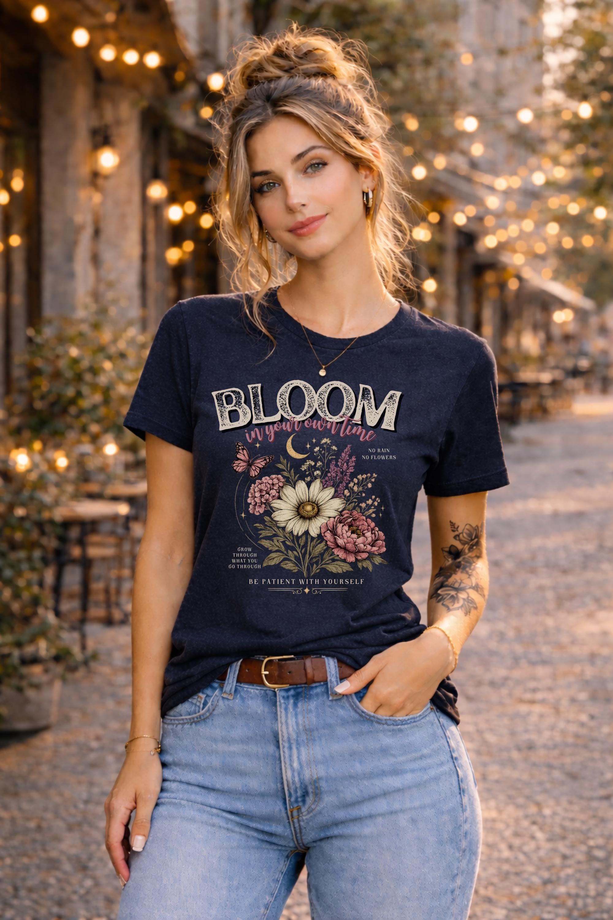 Woman wearing a floral inspirational t-shirt featuring the phrase "Bloom In Your Own Time" with vintage flowers, butterflies, moon accents, and self-love encouragement messages.