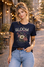 Woman wearing a floral inspirational t-shirt featuring the phrase "Bloom In Your Own Time" with vintage flowers, butterflies, moon accents, and self-love encouragement messages.