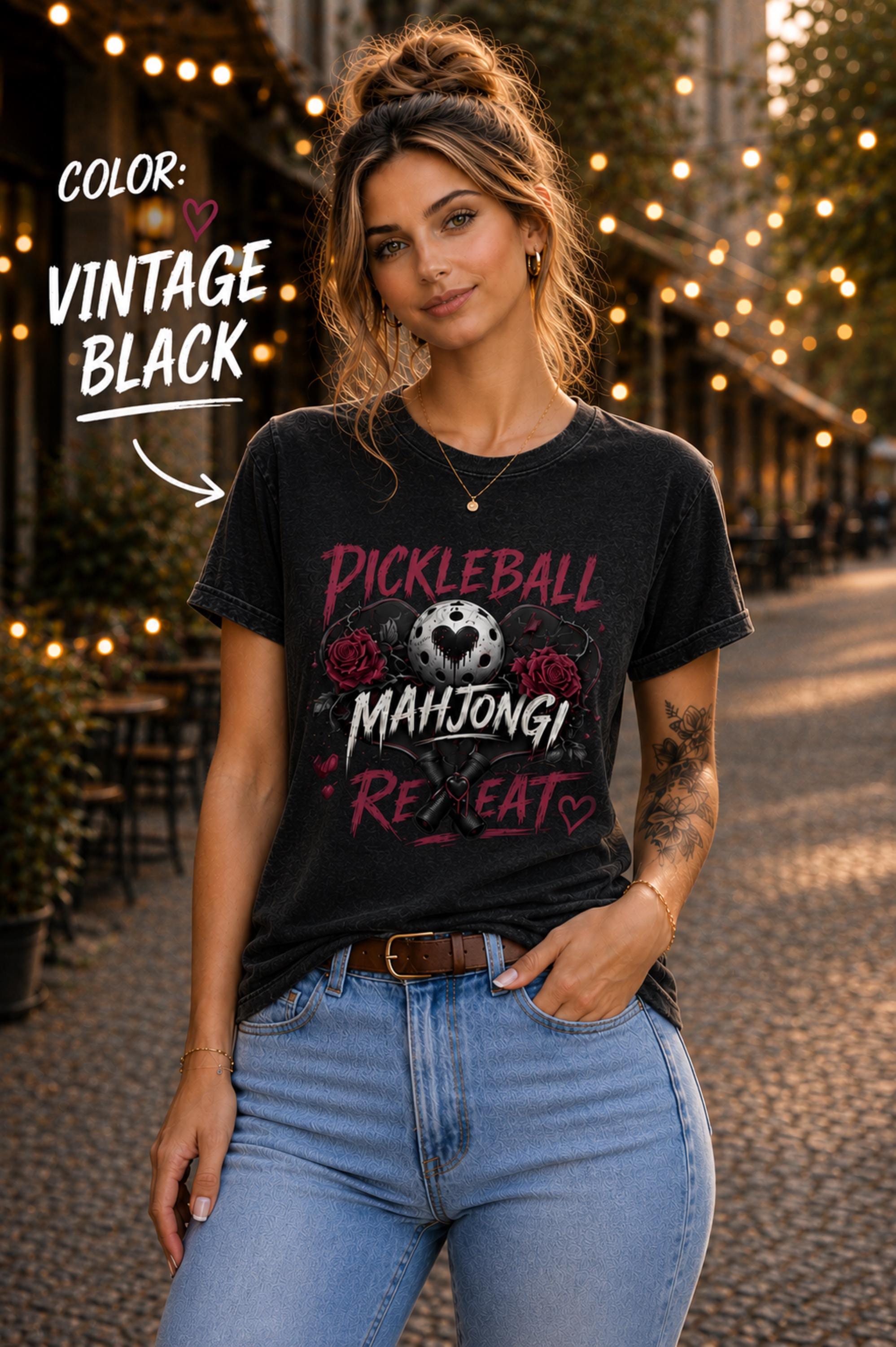 Short-sleeve t-shirt featuring a graphic print with the text PICKLEBALL MAHJONG REPEAT, a pickleball with a heart shape, two crossed pickleball paddles, and two dark red roses with small heart accents.