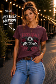 short-sleeve t-shirt featuring a graphic print with the text "PICKLEBALL MAHJONG REPEAT". The design includes a central pickleball with a heart cutout, flanked by two red roses, and two crossed pickleball paddles below.