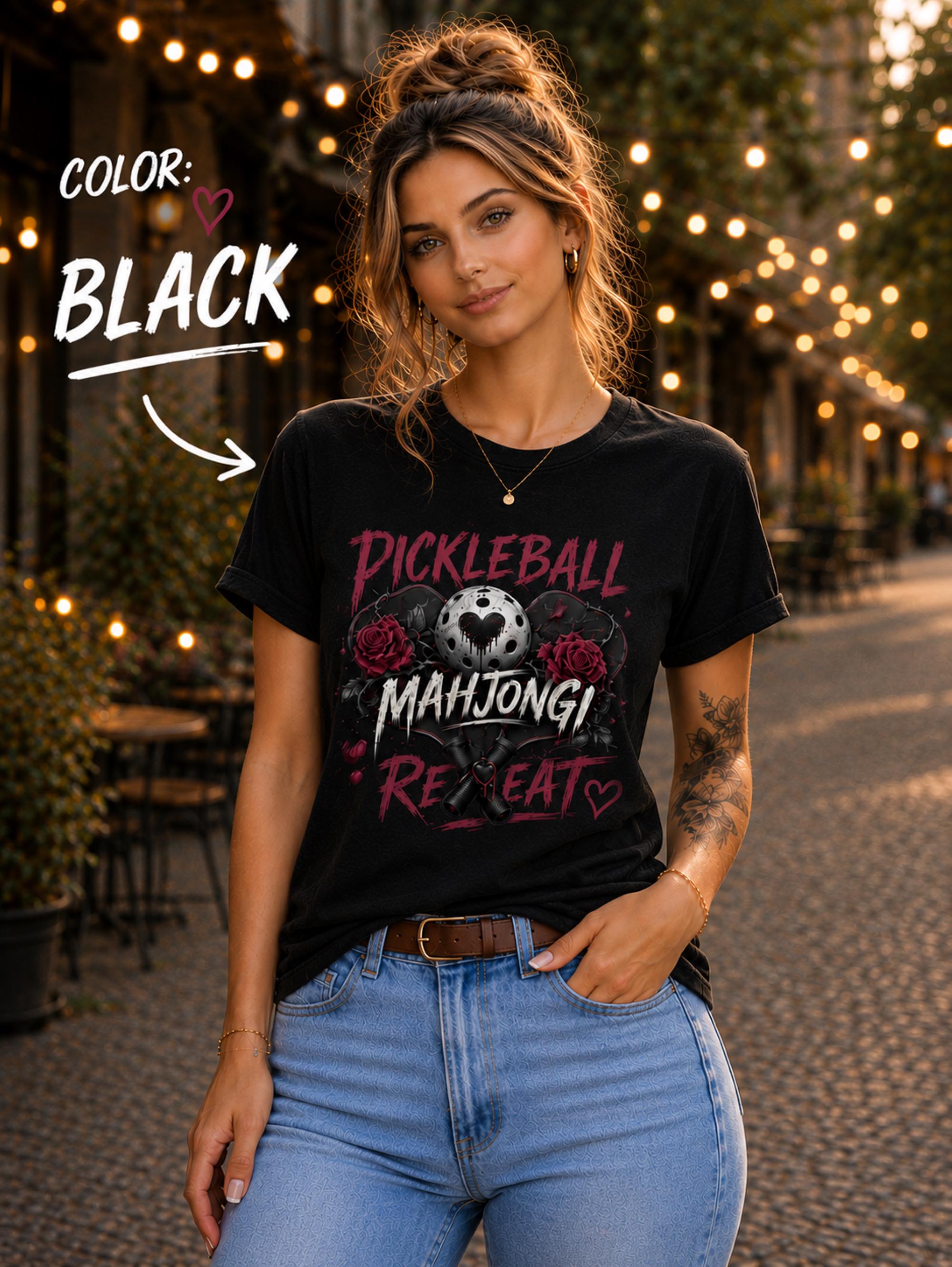 May include: A black short-sleeve t-shirt featuring a graphic print with the text "PICKLEBALL MAHJONG REPEAT". The design includes a central pickleball with a heart cutout, flanked by two red roses, and two crossed pickleball paddles below.