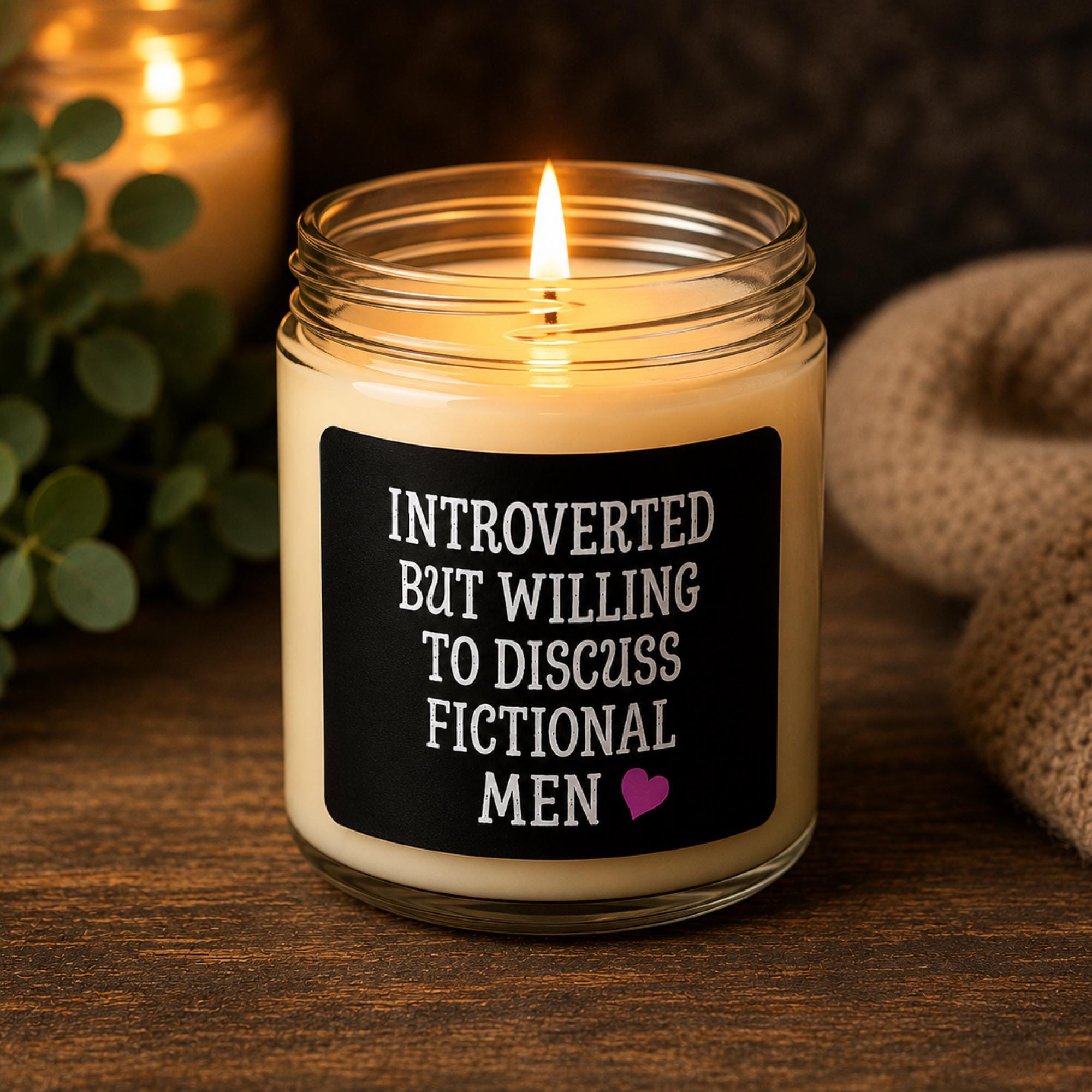 Dark romance themed scented soy candles featuring the phrase "Introverted But Willing To Discuss Fictional Men" displayed alongside gothic books and candlelit decor.
