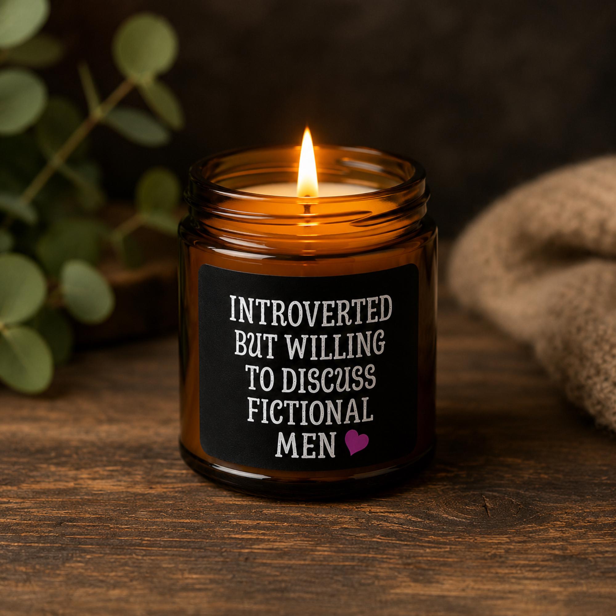 Dark romance themed scented soy candles featuring the phrase "Introverted But Willing To Discuss Fictional Men" displayed alongside gothic books and candlelit decor.