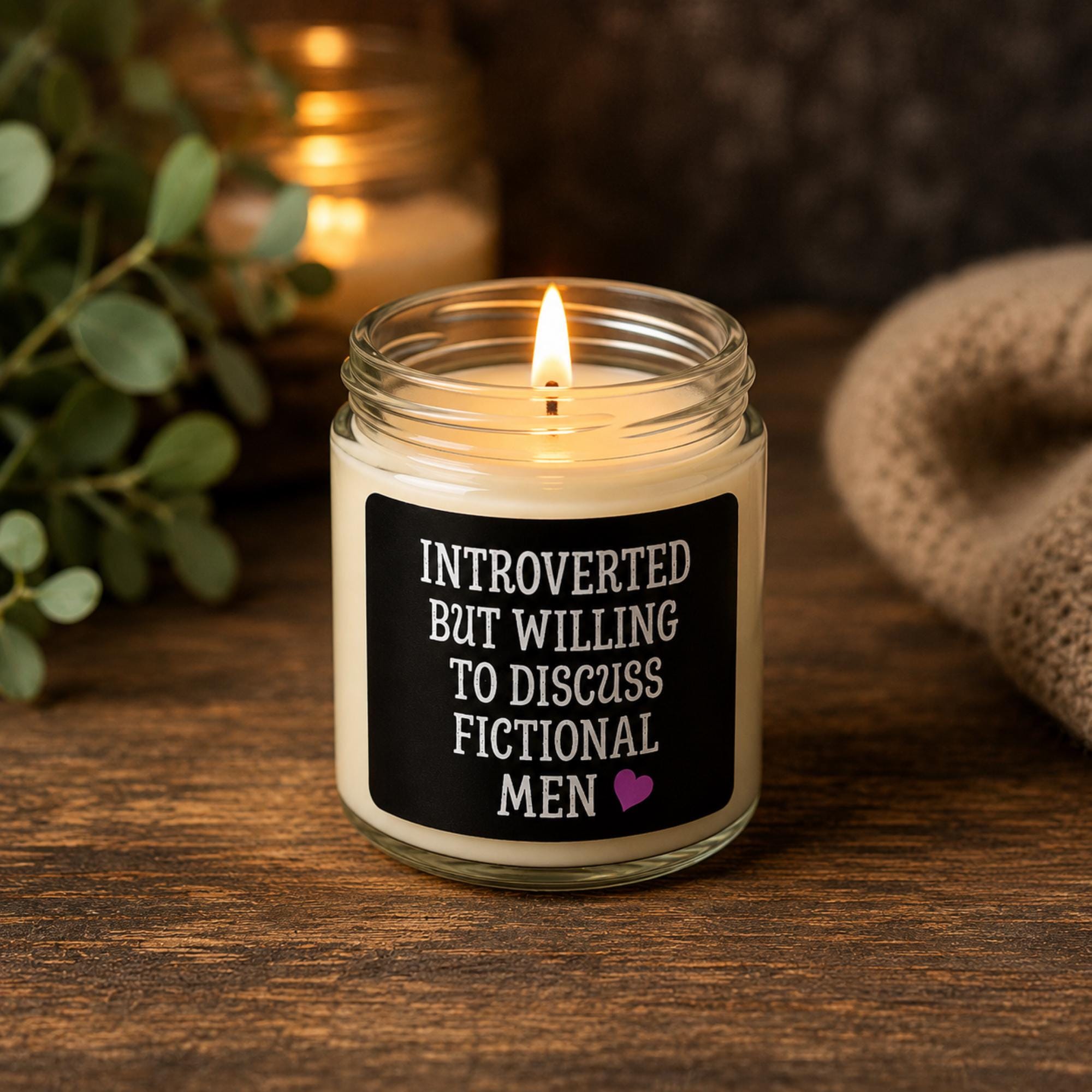 Dark romance themed scented soy candles featuring the phrase "Introverted But Willing To Discuss Fictional Men" displayed alongside gothic books and candlelit decor.