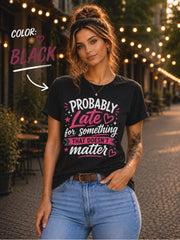 Woman wearing black graphic t-shirt featuring the phrase "Probably Late for Something That Doesn't Matter" in pink and white typography with playful heart accents.