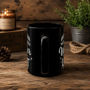 The handle of the Black ceramic mug featuring mountain artwork and the phrase "Not All Who Wander Are Lost" displayed in white typography on a cozy rustic background.
