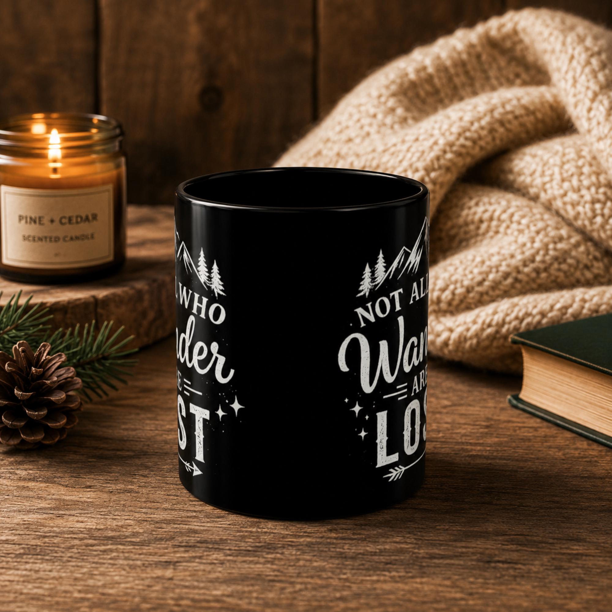 The front of the Black ceramic mug featuring mountain artwork and the phrase "Not All Who Wander Are Lost" displayed in white typography on a cozy rustic background.