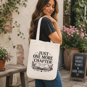 Woman carrying Just One More Chapter book lover tote bag outside bookstore café