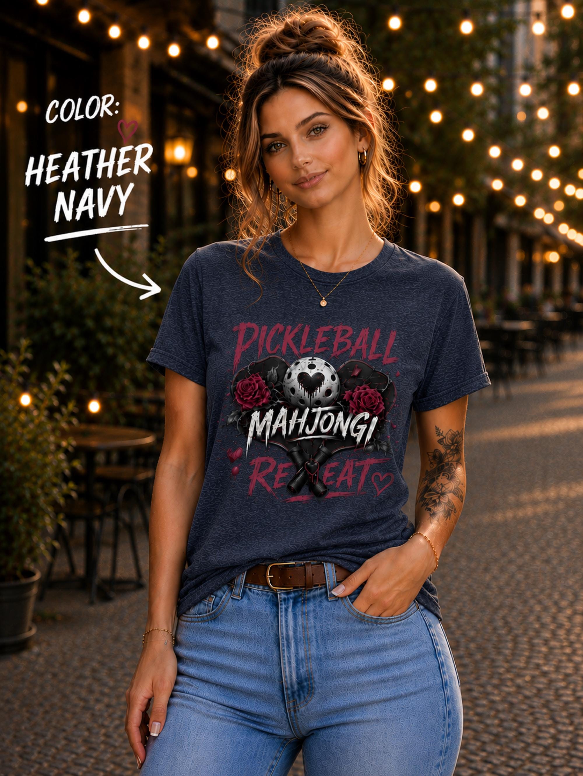 short-sleeve t-shirt featuring a graphic print with the text "PICKLEBALL MAHJONG REPEAT". The design includes a central pickleball with a heart cutout, flanked by two red roses, and two crossed pickleball paddles below.
