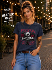 short-sleeve t-shirt featuring a graphic print with the text "PICKLEBALL MAHJONG REPEAT". The design includes a central pickleball with a heart cutout, flanked by two red roses, and two crossed pickleball paddles below.