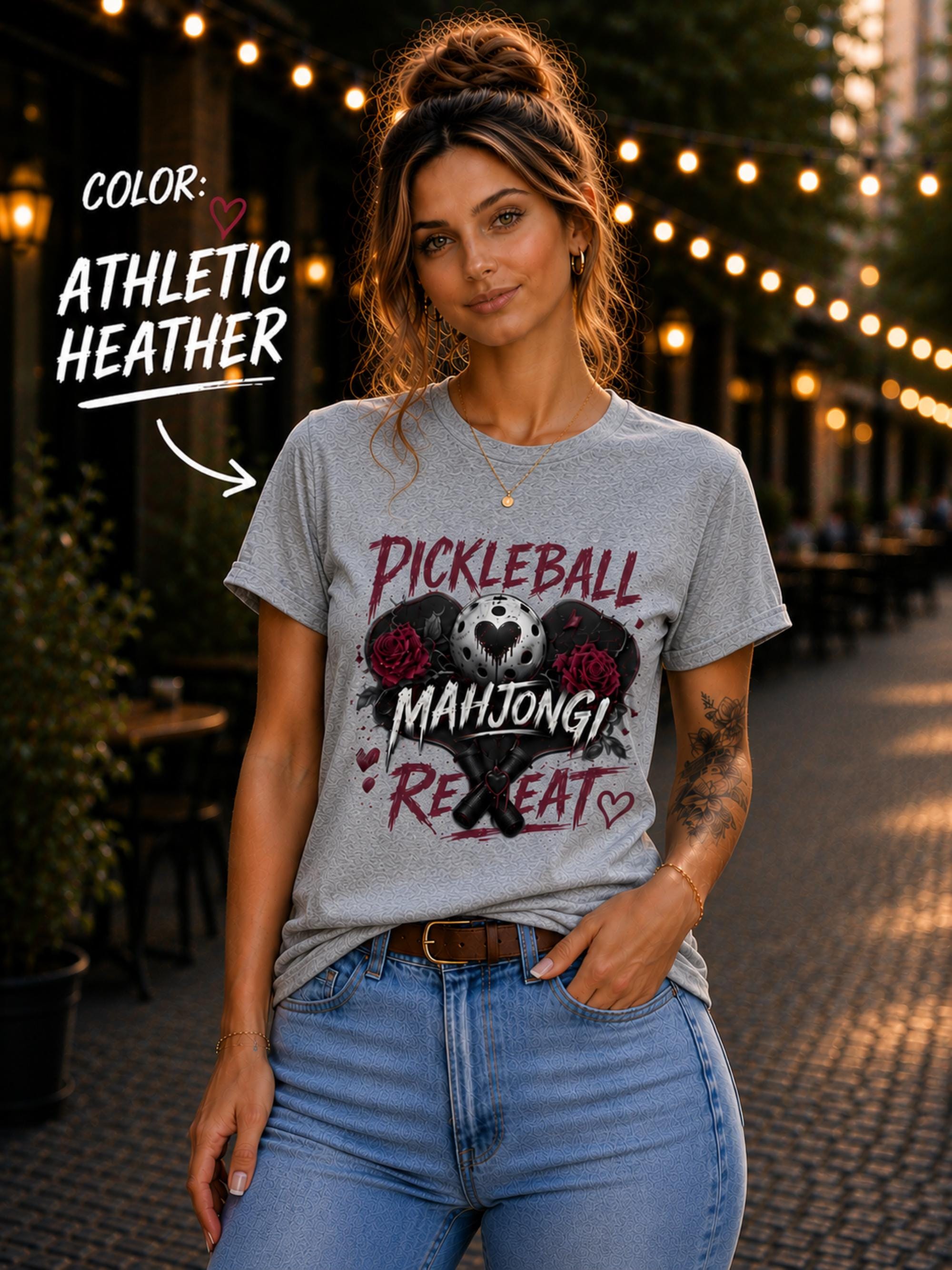 short-sleeve t-shirt featuring a graphic print with the text "PICKLEBALL MAHJONG REPEAT". The design includes a central pickleball with a heart cutout, flanked by two red roses, and two crossed pickleball paddles below.
