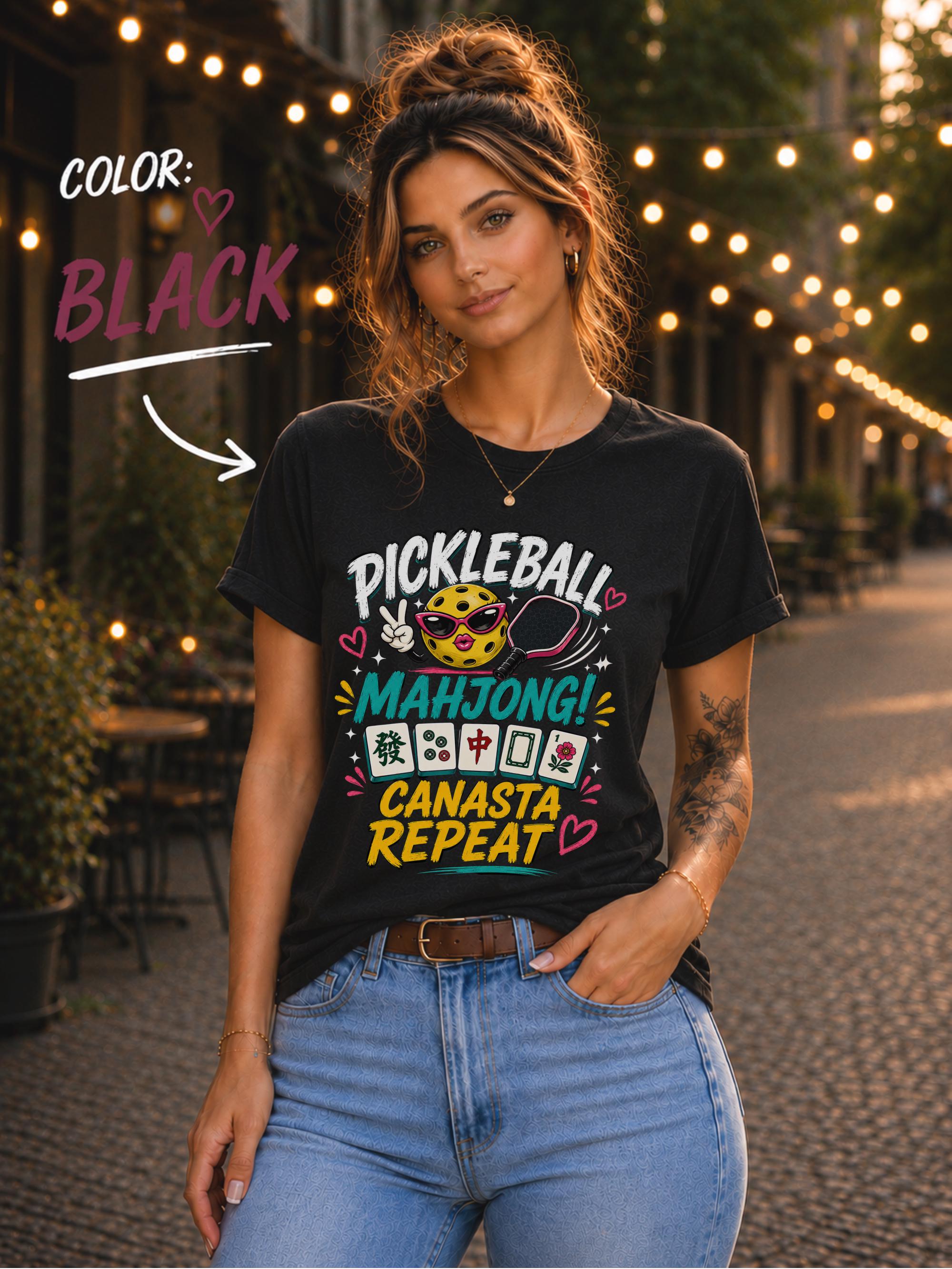 Woman wearing a black graphic t-shirt featuring the colorful phrase "Pickleball Mahjong Canasta Repeat" with a smiling pickleball character, paddle, and Mahjong tiles, styled for casual everyday wear.