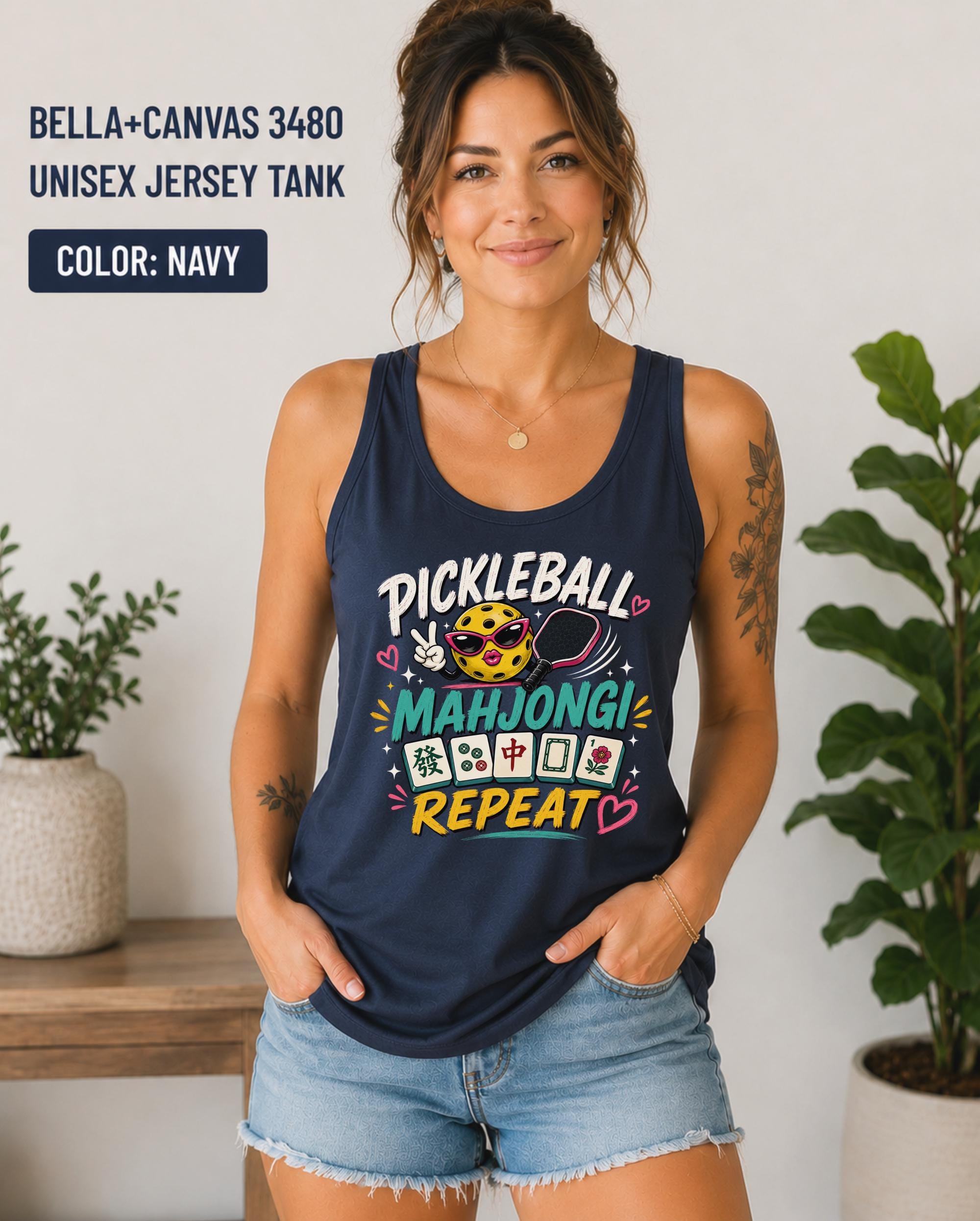 Woman wearing a navy Bella+Canvas 3480 unisex jersey tank featuring a colorful "Pickleball Mahjong Repeat" graphic with a smiling pickleball, paddle, Mahjong tiles, and bright playful lettering.