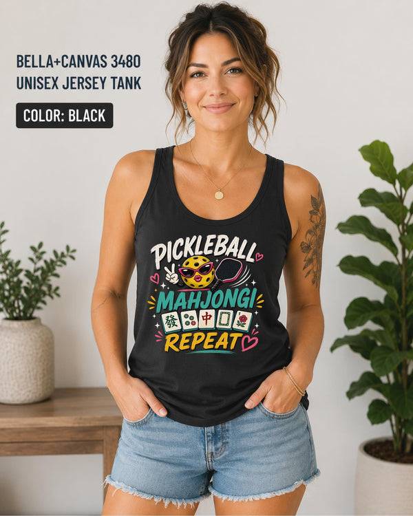 Woman wearing a black Bella+Canvas 3480 unisex jersey tank featuring a colorful "Pickleball Mahjong Repeat" graphic with a smiling pickleball, paddle, Mahjong tiles, and bright playful lettering.
