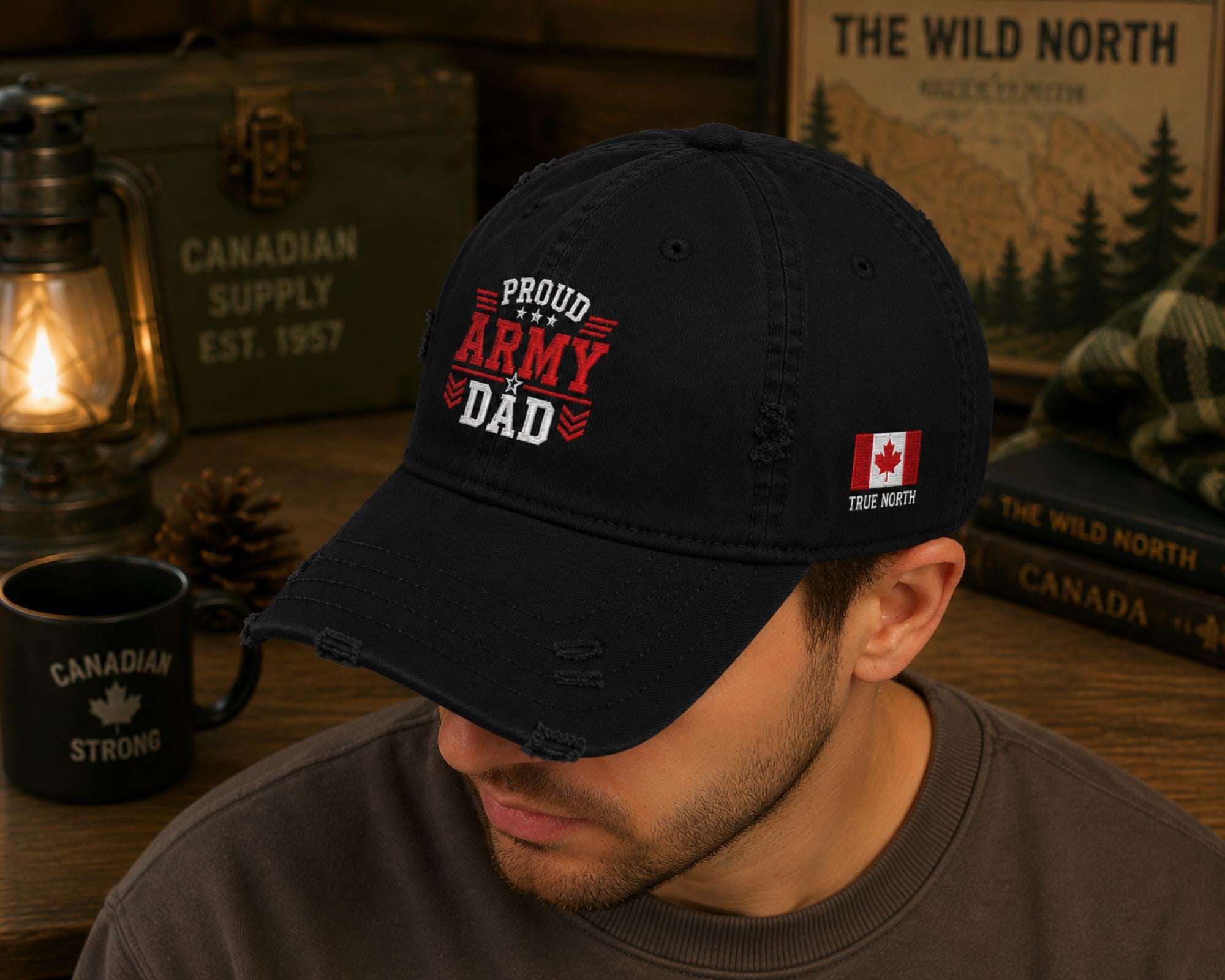 Black distressed embroidered dad hat featuring a bold "Proud Army Dad" design on the front with a red maple leaf and "EH!" embroidery on the side, styled in a rustic outdoor setting with camping accessories.