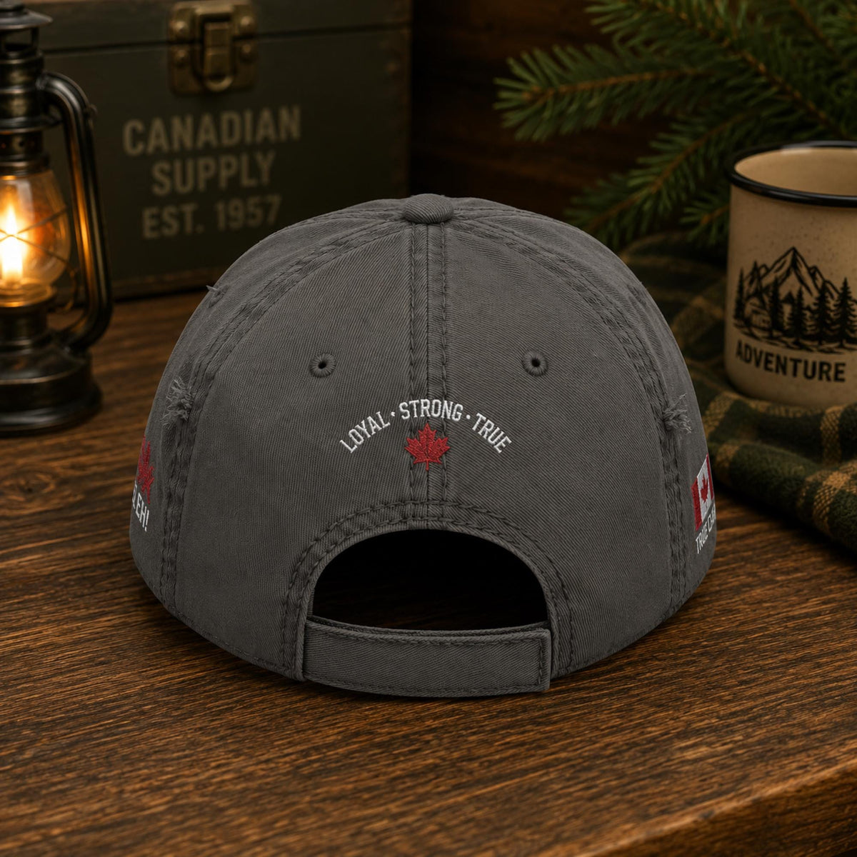 Charcoal distressed embroidered dad hat featuring "Proud Canadian Strong & Free" on the front with maple leaf accents, Canadian flag embroidery on the sides, and an EH! True North maple leaf detail in a rustic outdoor setting.
