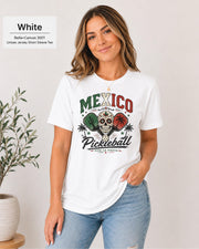 Woman wearing a White Bella+Canvas 3001 T-shirt featuring a colorful Mexico Pickleball sugar skull design with cactus, paddles, palm trees, and "Viva La Fiesta" text.