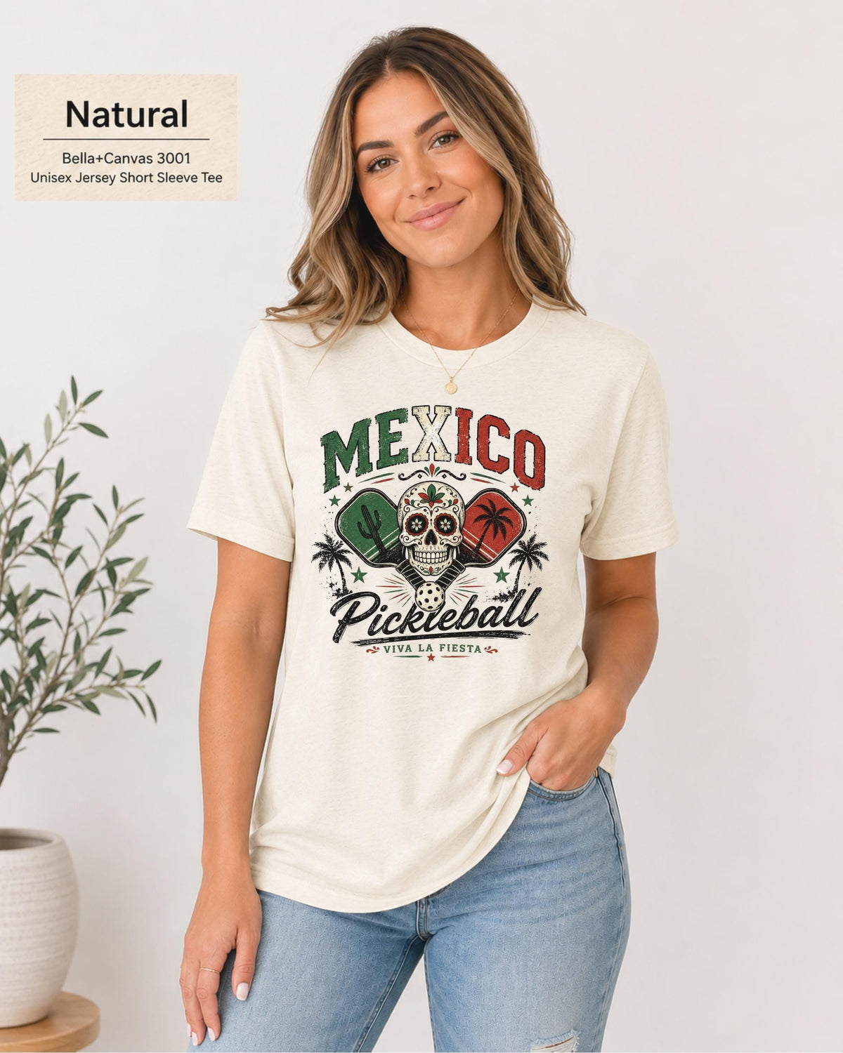 Woman wearing a Natural Bella+Canvas 3001 T-shirt featuring a colorful Mexico Pickleball sugar skull design with cactus, paddles, palm trees, and "Viva La Fiesta" text.