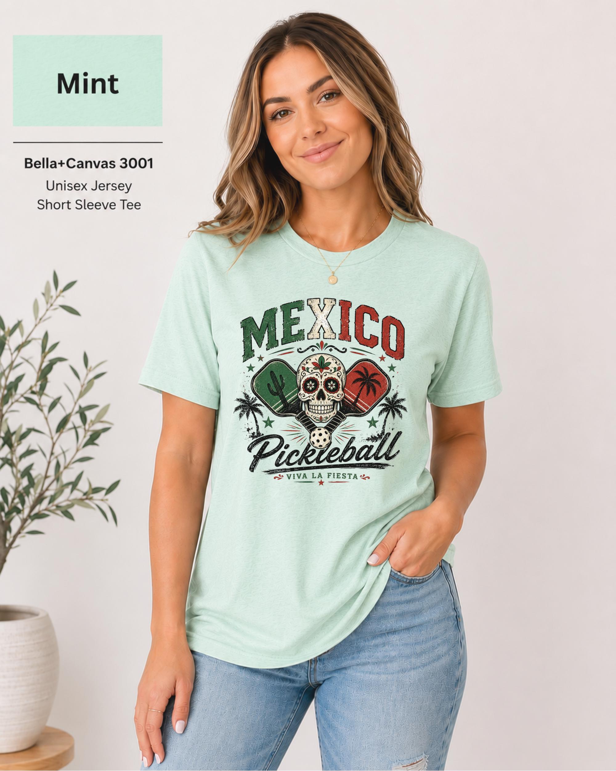 Woman wearing a  Mint Bella+Canvas 3001 T-shirt featuring a colorful Mexico Pickleball sugar skull design with cactus, paddles, palm trees, and "Viva La Fiesta" text.