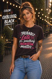 Woman wearing Oxblood black graphic t-shirt featuring the phrase "Probably Late for Something That Doesn't Matter" in pink and white typography with playful heart accents.