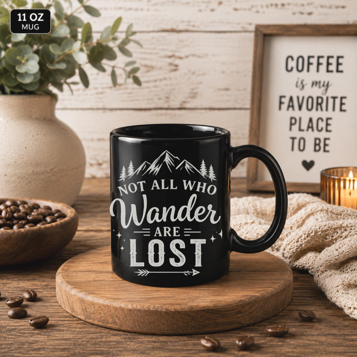 Black ceramic mug featuring mountain artwork and the phrase "Not All Who Wander Are Lost" displayed in white typography on a cozy rustic background.