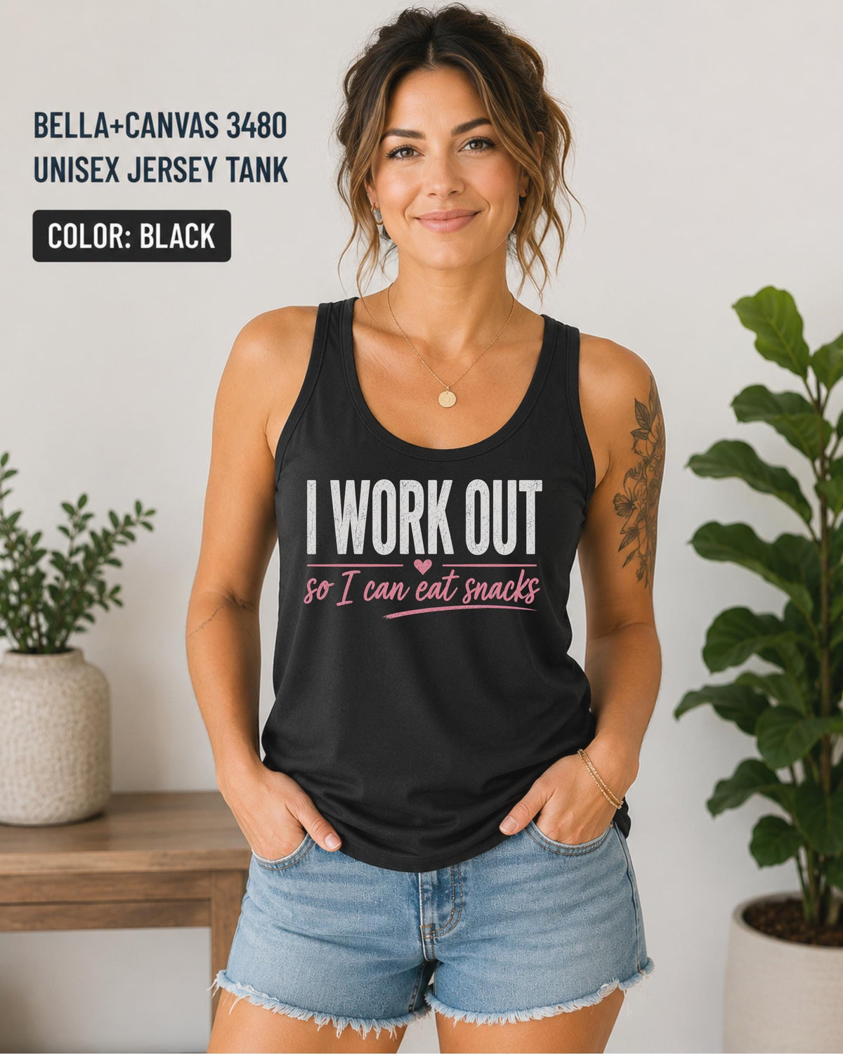 Woman wearing a black Bella+Canvas jersey tank featuring the phrase "I Work Out So I Can Eat Snacks" in white and pink lettering.