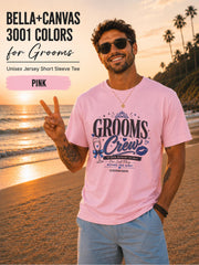 Bella+Canvas 3001 Pink groom crew shirt featuring a blue wedding party design with champagne glass, crown, kiss mark, and customizable wedding date for bachelor party celebrations.