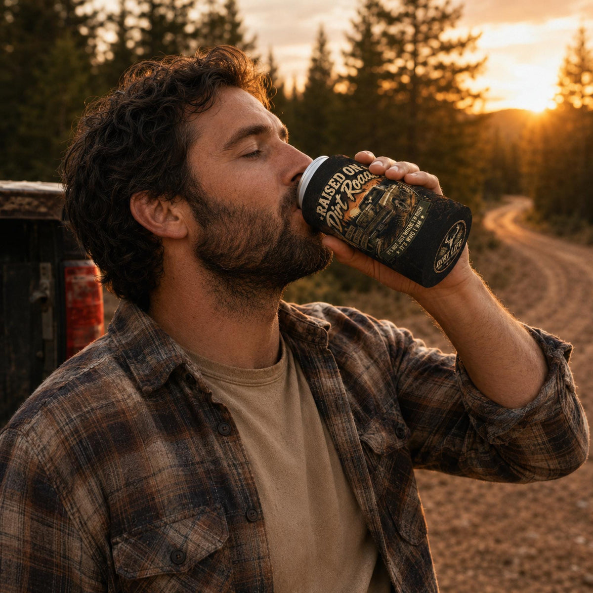 Man enjoying a drink outdoors at sunset while holding a "Raised on Dirt Roads" can cooler featuring a vintage pickup truck design, perfect for country living, camping, hunting, and rural lifestyle gifts.
