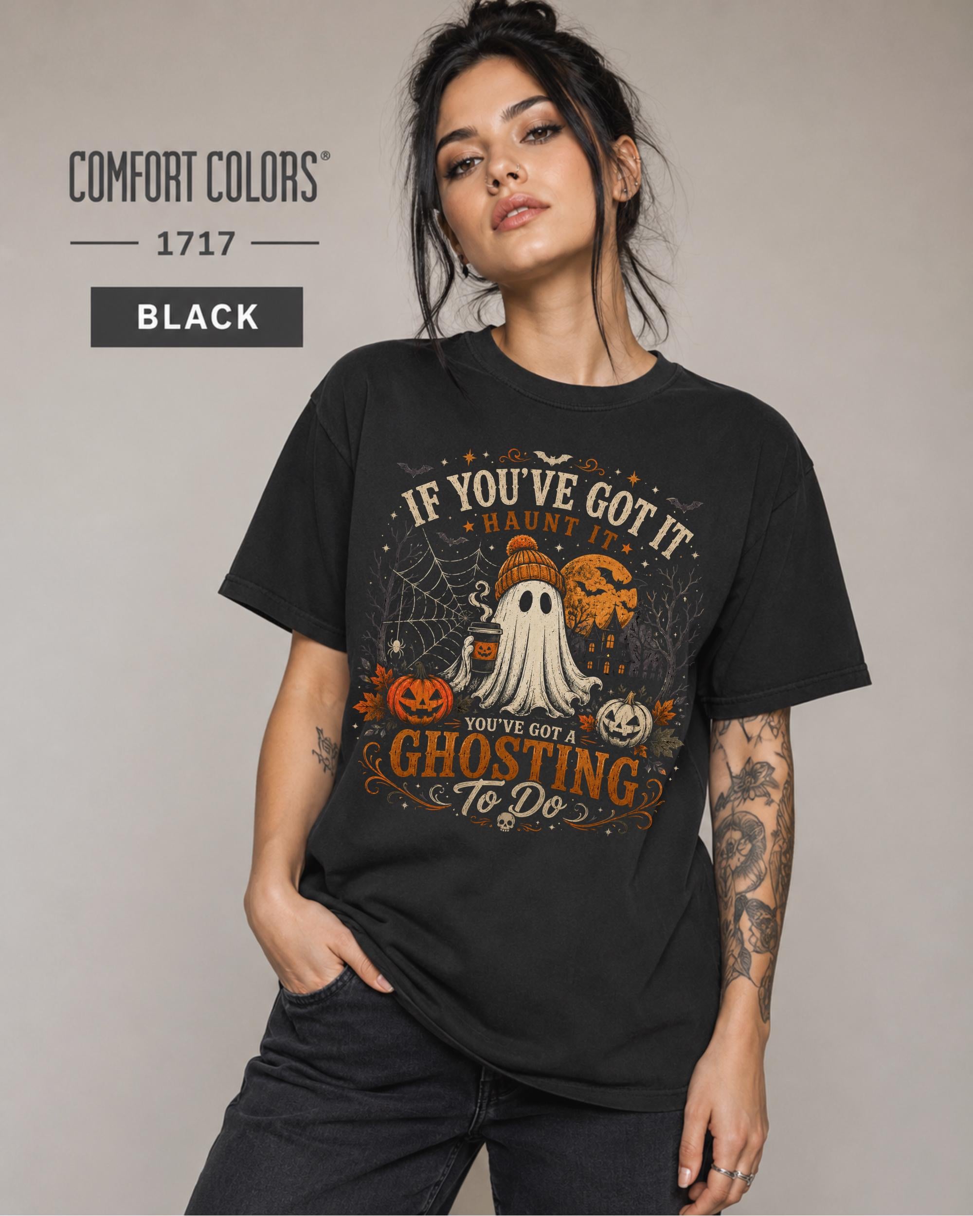 Woman wearing a Comfort Colors 1717 Black T-shirt featuring a vintage Halloween ghost design with pumpkins, spiderwebs, haunted house, moon, bats, and the funny quote "If You've Got It Haunt It... You've Got a Ghosting To Do."
