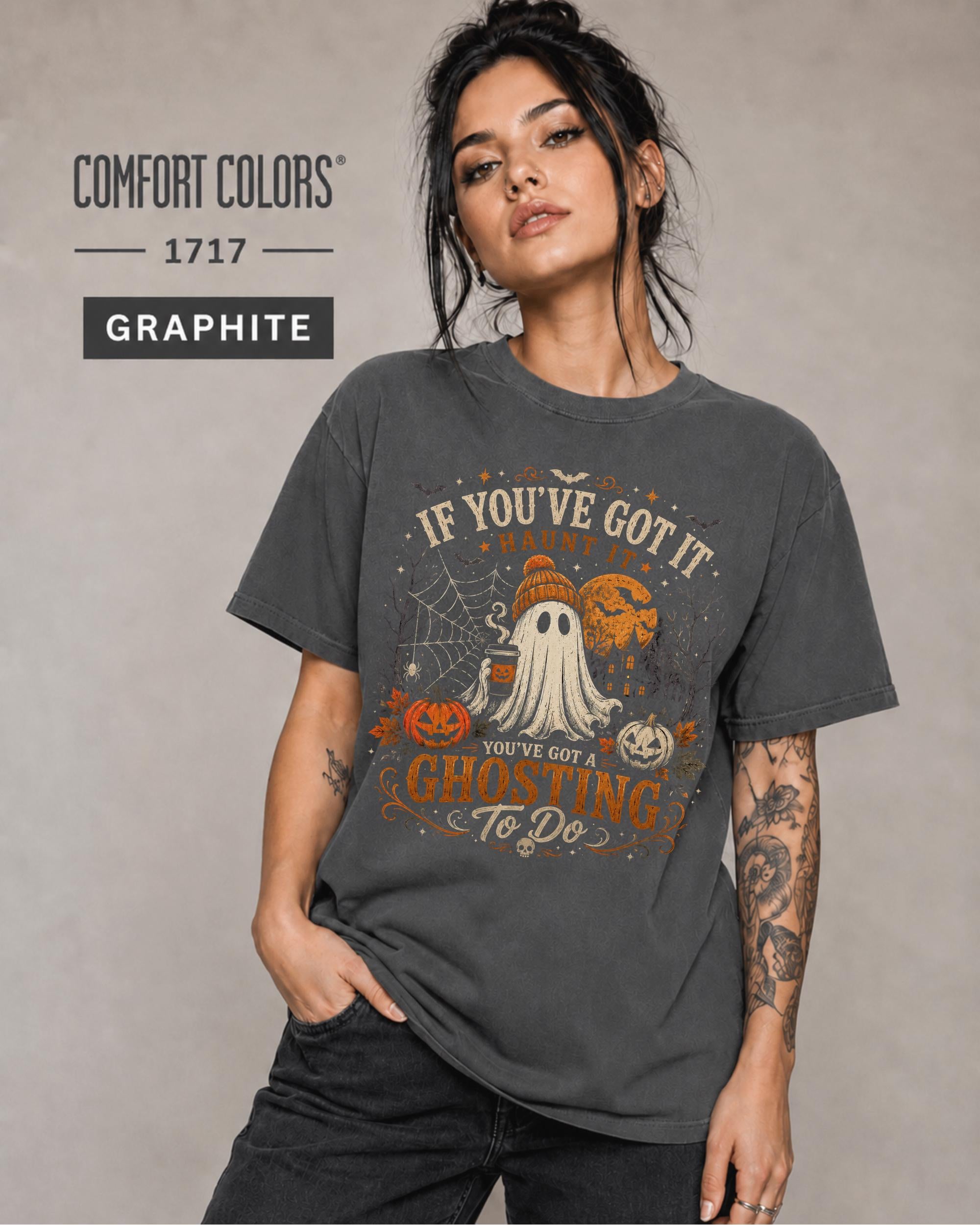 Woman wearing a Comfort Colors 1717 Graphite T-shirt featuring a vintage Halloween ghost design with pumpkins, spiderwebs, haunted house, moon, bats, and the funny quote "If You've Got It Haunt It... You've Got a Ghosting To Do."