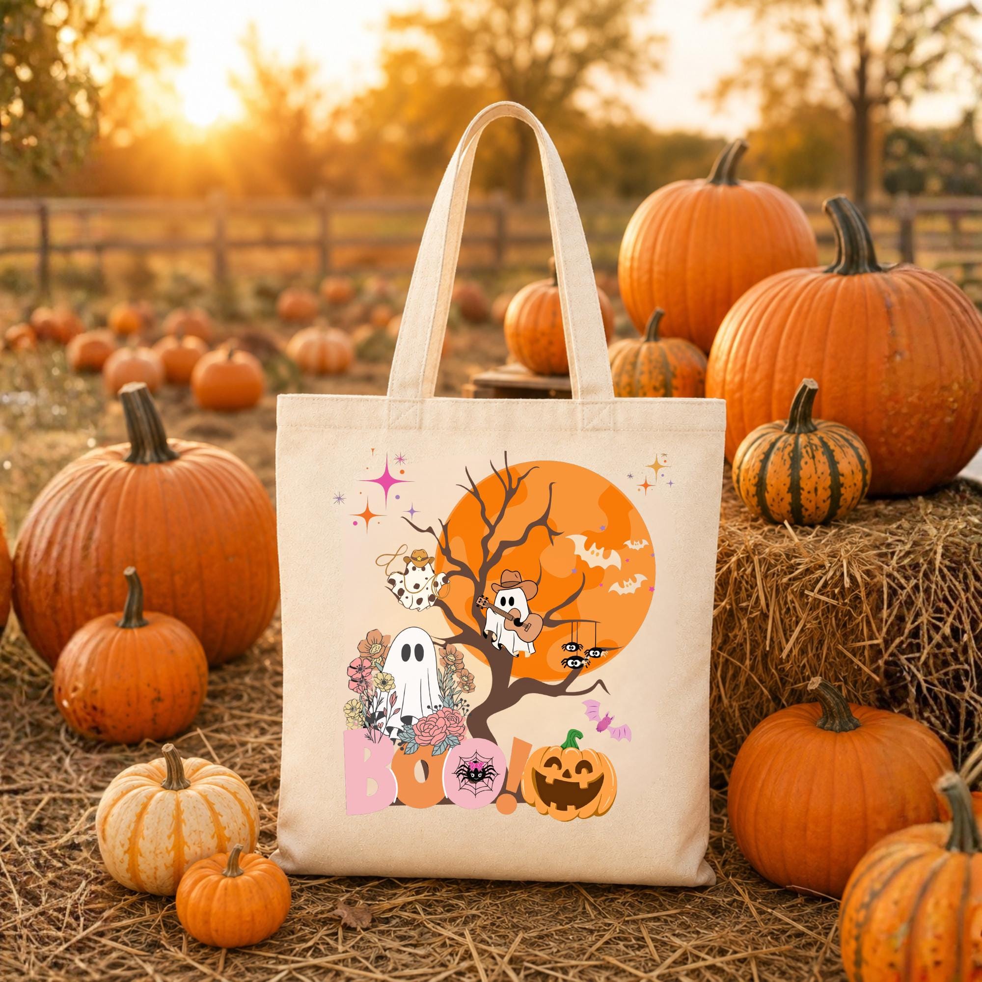 Tan tote bag with a Halloween design featuring a ghost, a pumpkin, and bats in front of a full moon. The text "BOO!" is printed on the bag.