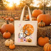 Tan tote bag with a Halloween design featuring a ghost, a pumpkin, and bats in front of a full moon. The text "BOO!" is printed on the bag.