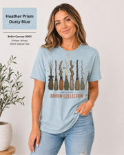 Bella+Canvas 3001 Heather Prism Dusty Blue unisex t-shirt featuring a vintage Broom Collection graphic with illustrated witch brooms, earthy autumn colors, and cozy Halloween-inspired artwork.