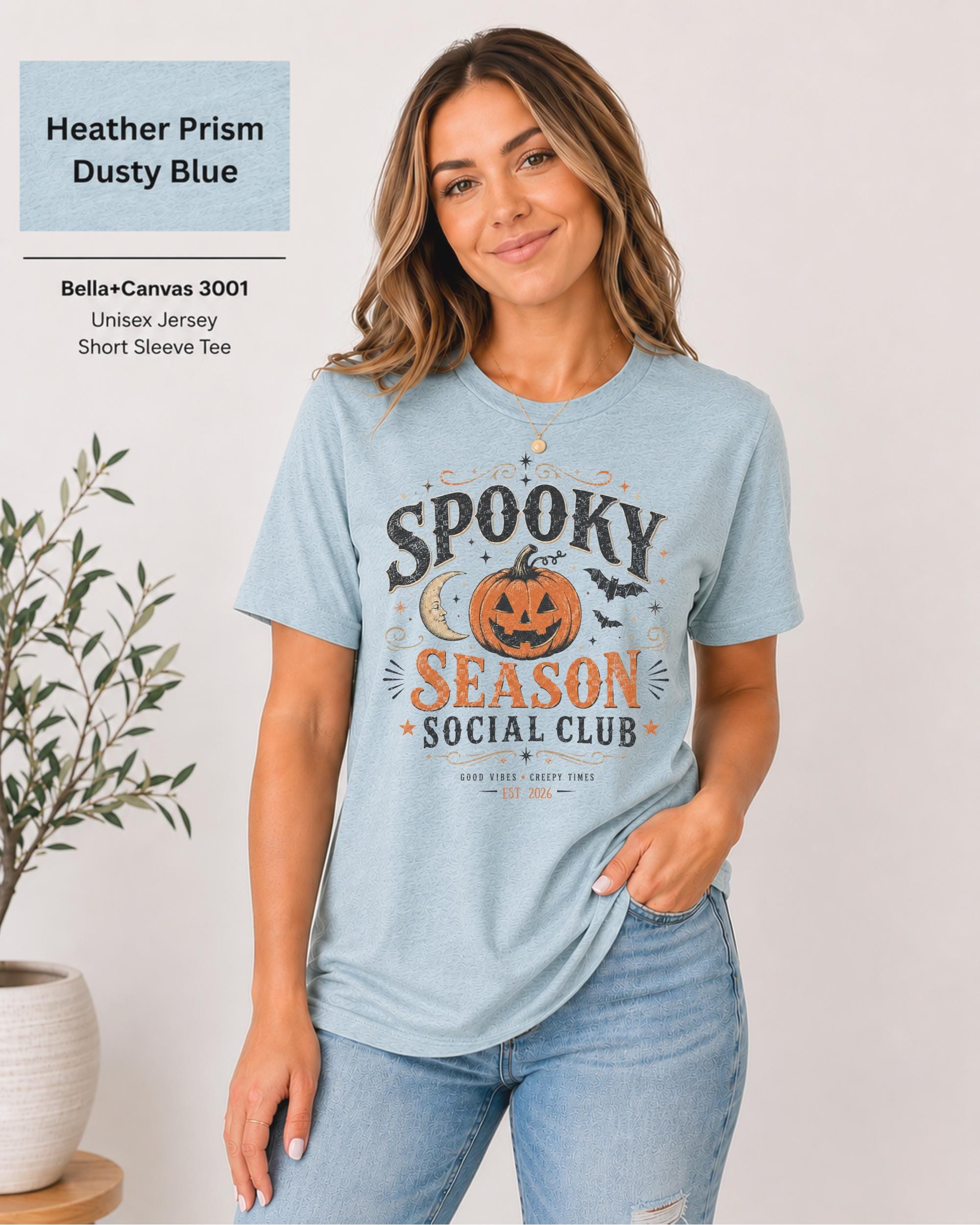 Bella+Canvas 3001 Heather Prism Dusty Blue unisex t-shirt featuring a vintage "Spooky Season Social Club" graphic with a smiling pumpkin, crescent moon, bats, and distressed autumn typography for Halloween and fall.