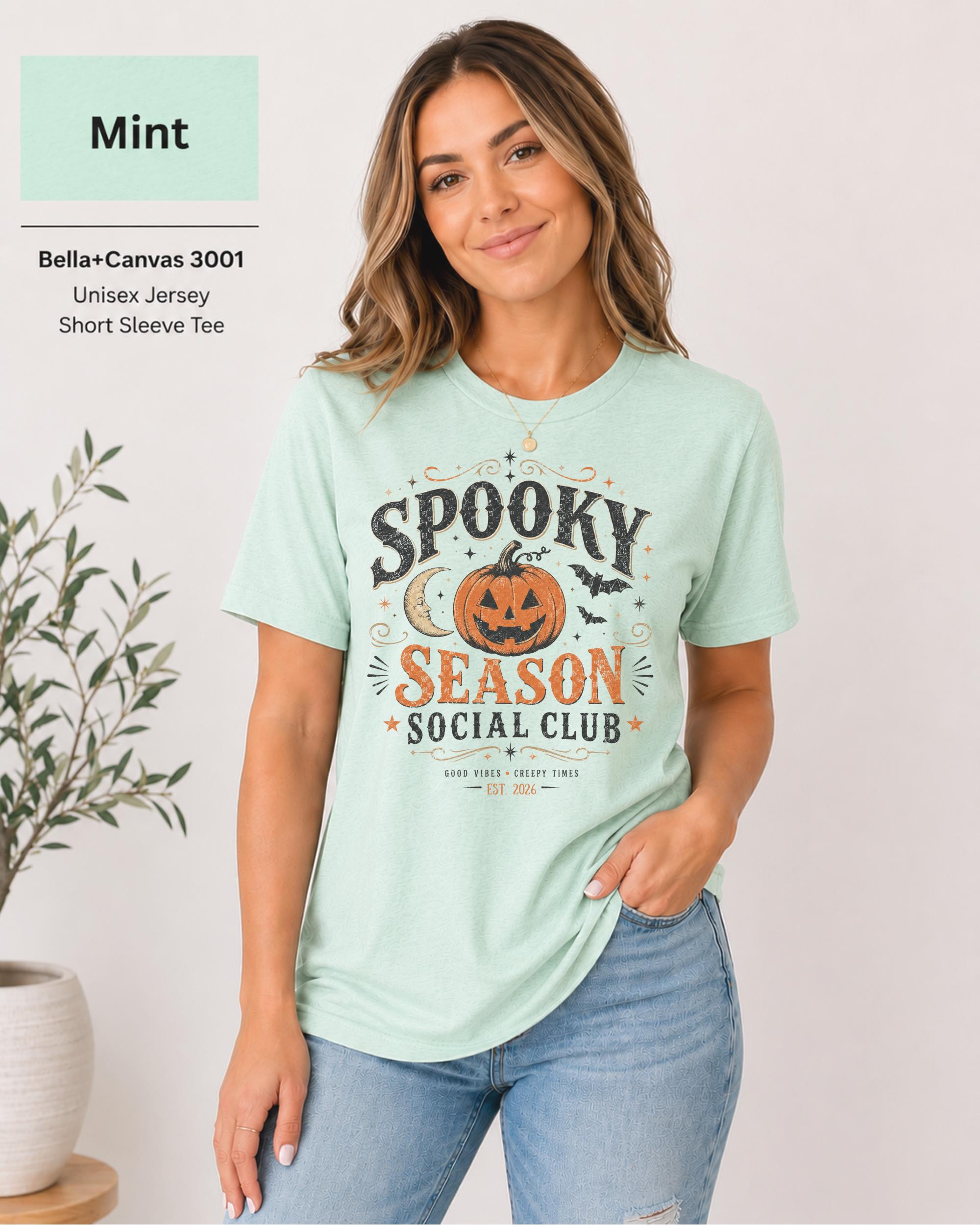Bella+Canvas 3001 Mint unisex t-shirt featuring a vintage "Spooky Season Social Club" graphic with a smiling pumpkin, crescent moon, bats, and distressed autumn typography for Halloween and fall.