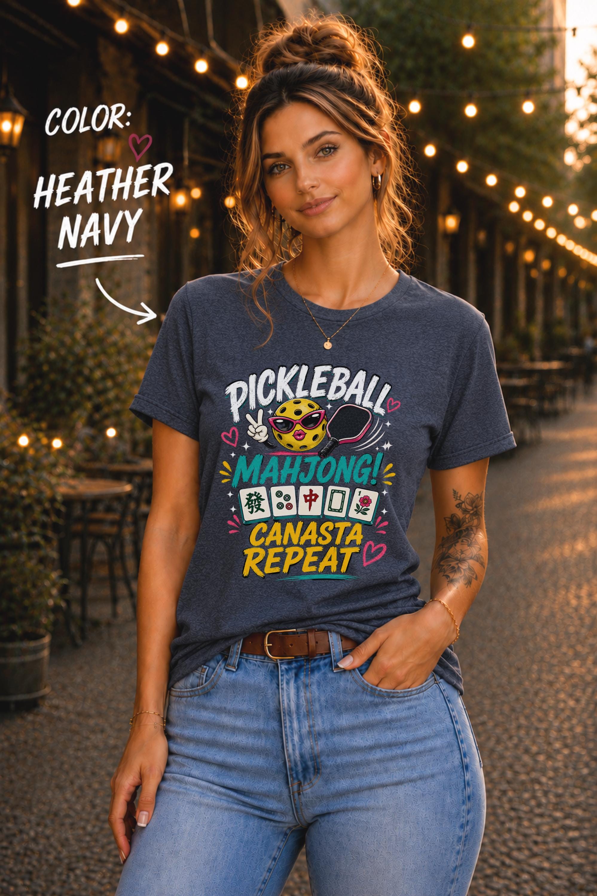 Woman wearing a heather navy graphic t-shirt featuring the colorful phrase "Pickleball Mahjong Canasta Repeat" with a smiling pickleball character, paddle, and Mahjong tiles, styled for casual everyday wear.