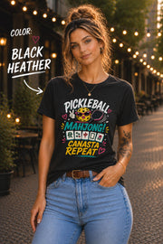 Woman wearing a black heather graphic t-shirt featuring the colorful phrase "Pickleball Mahjong Canasta Repeat" with a smiling pickleball character, paddle, and Mahjong tiles, styled for casual everyday wear.