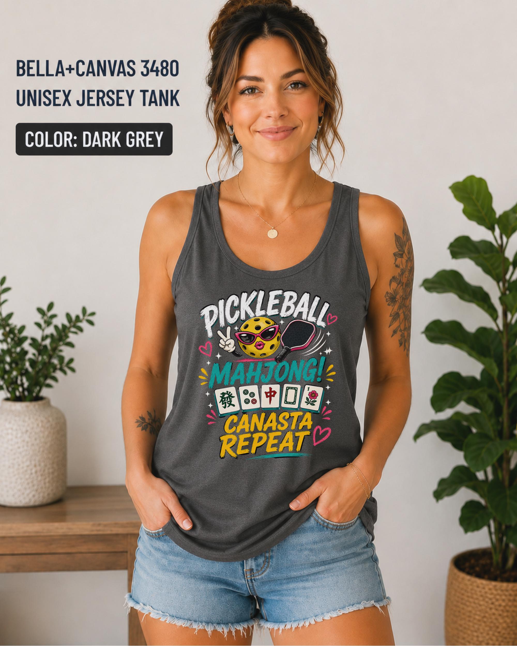 Woman wearing a dark grey Bella+Canvas 3480 jersey tank featuring a colorful "Pickleball Mahjong Canasta Repeat" graphic with a smiling pickleball character, paddle, and Mahjong tiles.