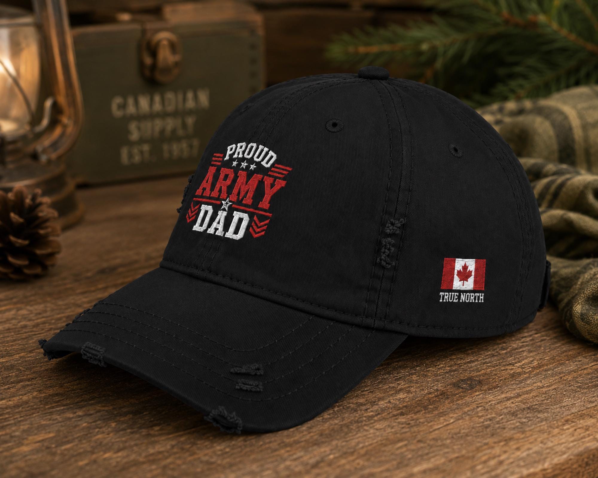 Black distressed embroidered dad hat featuring a bold "Proud Army Dad" design on the front with a red maple leaf and "EH!" "True North" embroidery on the side, styled in a rustic outdoor setting with camping accessories.