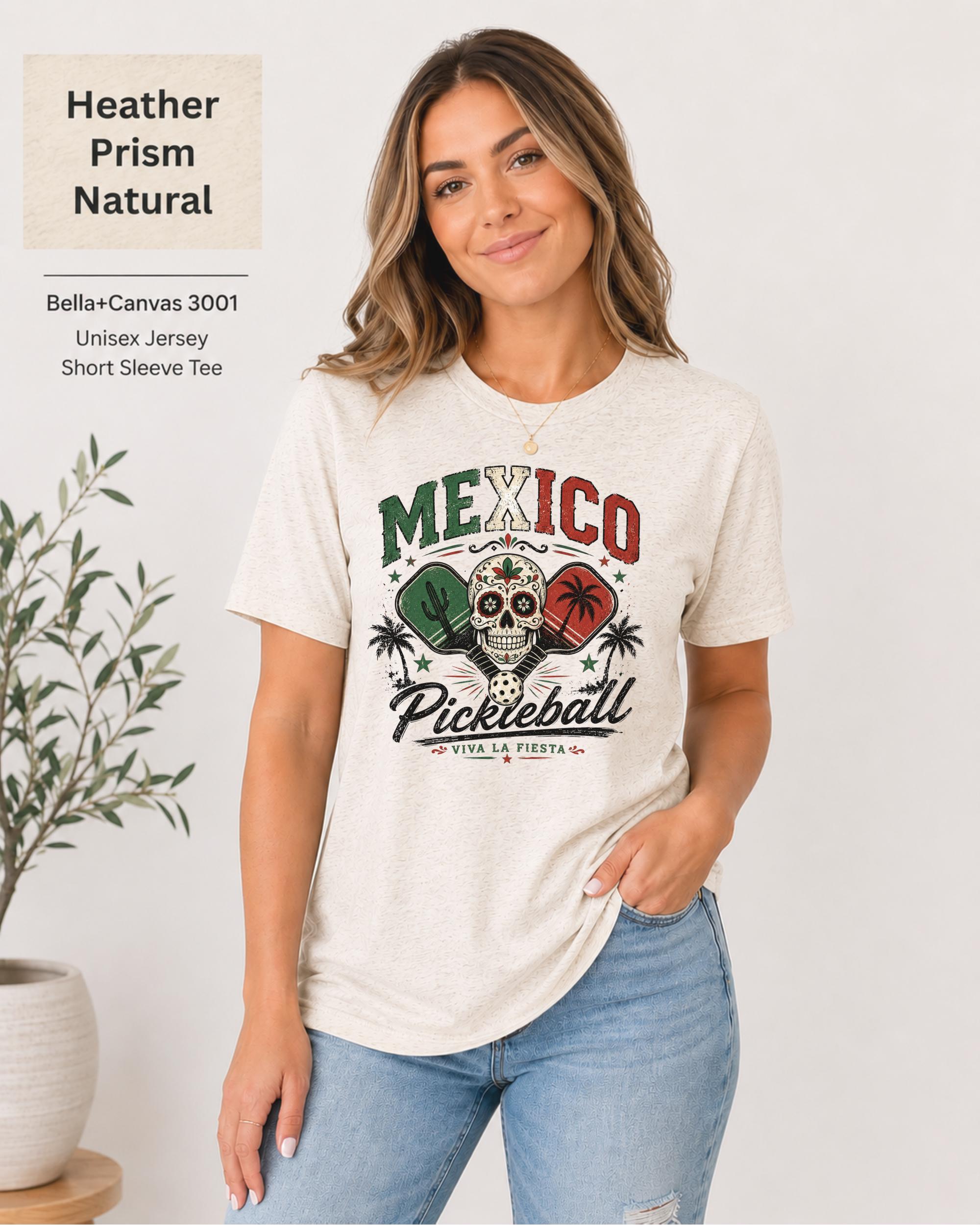 Woman wearing a Heather Prism Natural Bella+Canvas 3001 T-shirt featuring a colorful Mexico Pickleball sugar skull design with cactus, paddles, palm trees, and "Viva La Fiesta" text.