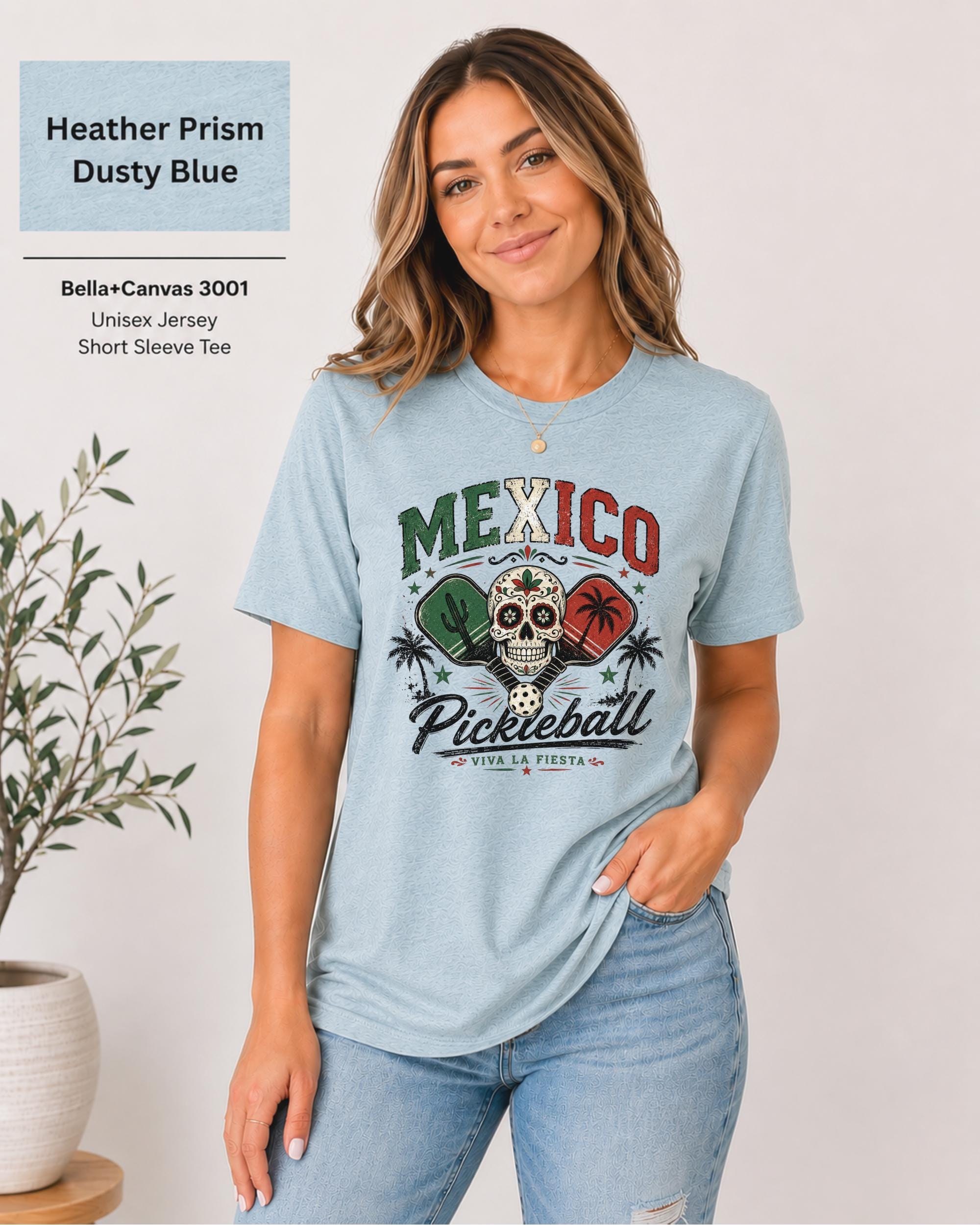 Woman wearing a Heather Prism Dusty blue Bella+Canvas 3001 T-shirt featuring a colorful Mexico Pickleball sugar skull design with cactus, paddles, palm trees, and "Viva La Fiesta" text.