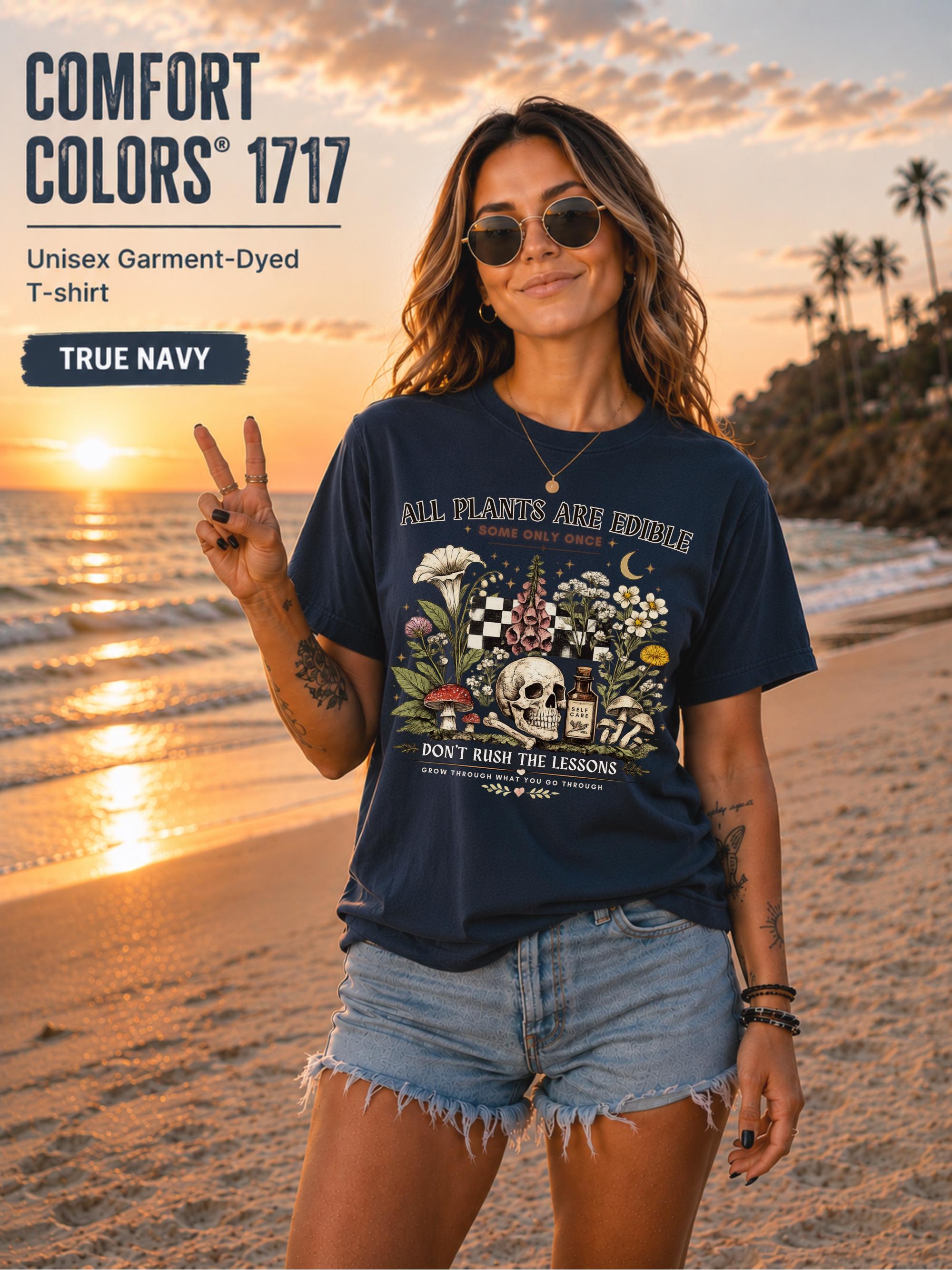 Woman wearing a true navy Comfort Colors 1717 garment-dyed T-shirt featuring a vintage botanical skull design with mushrooms, flowers, and the quote "All Plants Are Edible... Some Only Once" on a beach at sunset.