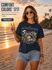 Woman wearing a true navy Comfort Colors 1717 garment-dyed T-shirt featuring a vintage botanical skull design with mushrooms, flowers, and the quote "All Plants Are Edible... Some Only Once" on a beach at sunset.