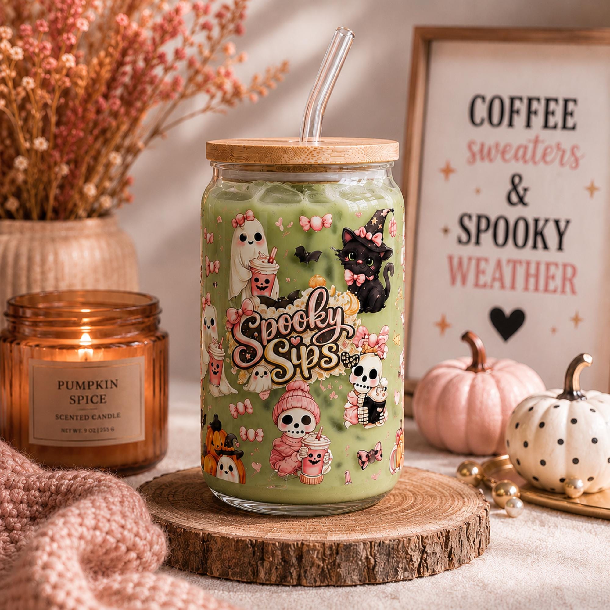 Cute spooky Halloween glass tumbler with ghost, black cat, skeleton, pink bows and Spooky Sips design on a cozy fall display.