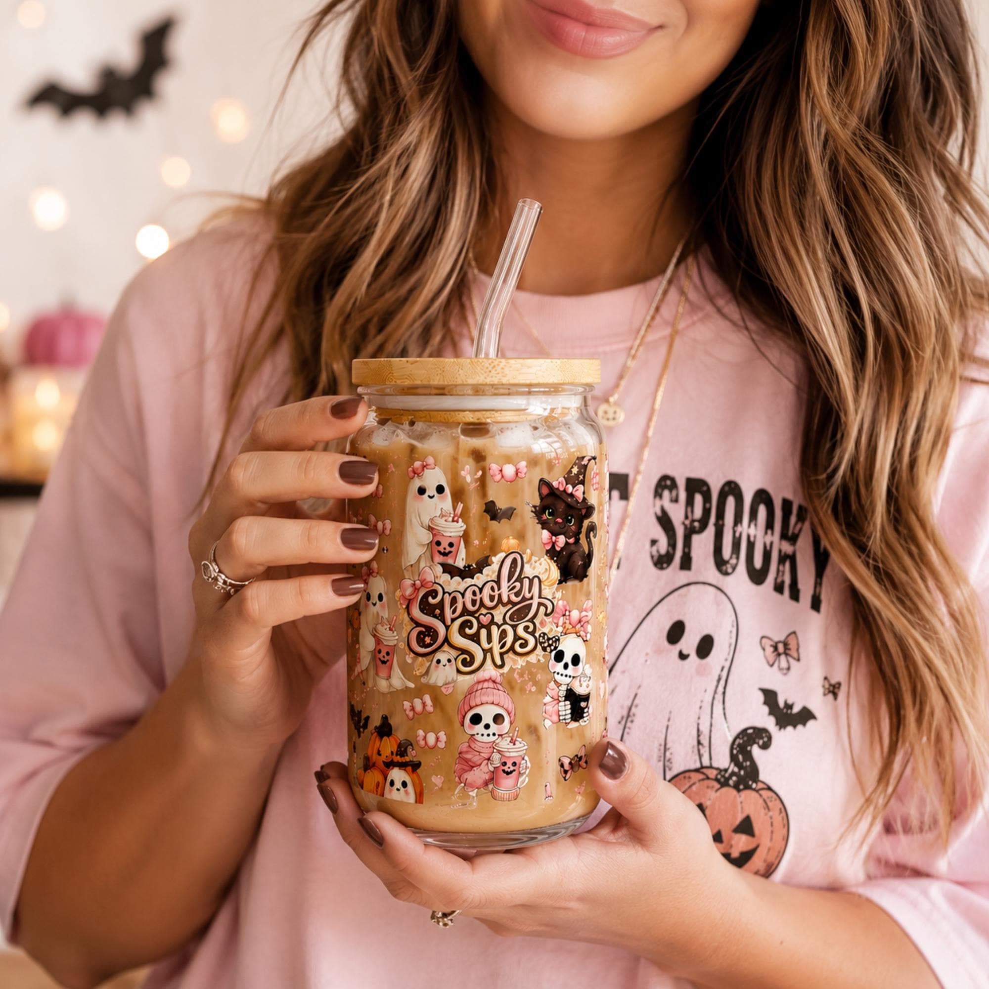 Woman holding a cute Halloween glass tumbler filled with iced coffee featuring ghost, black cat and pumpkin artwork.