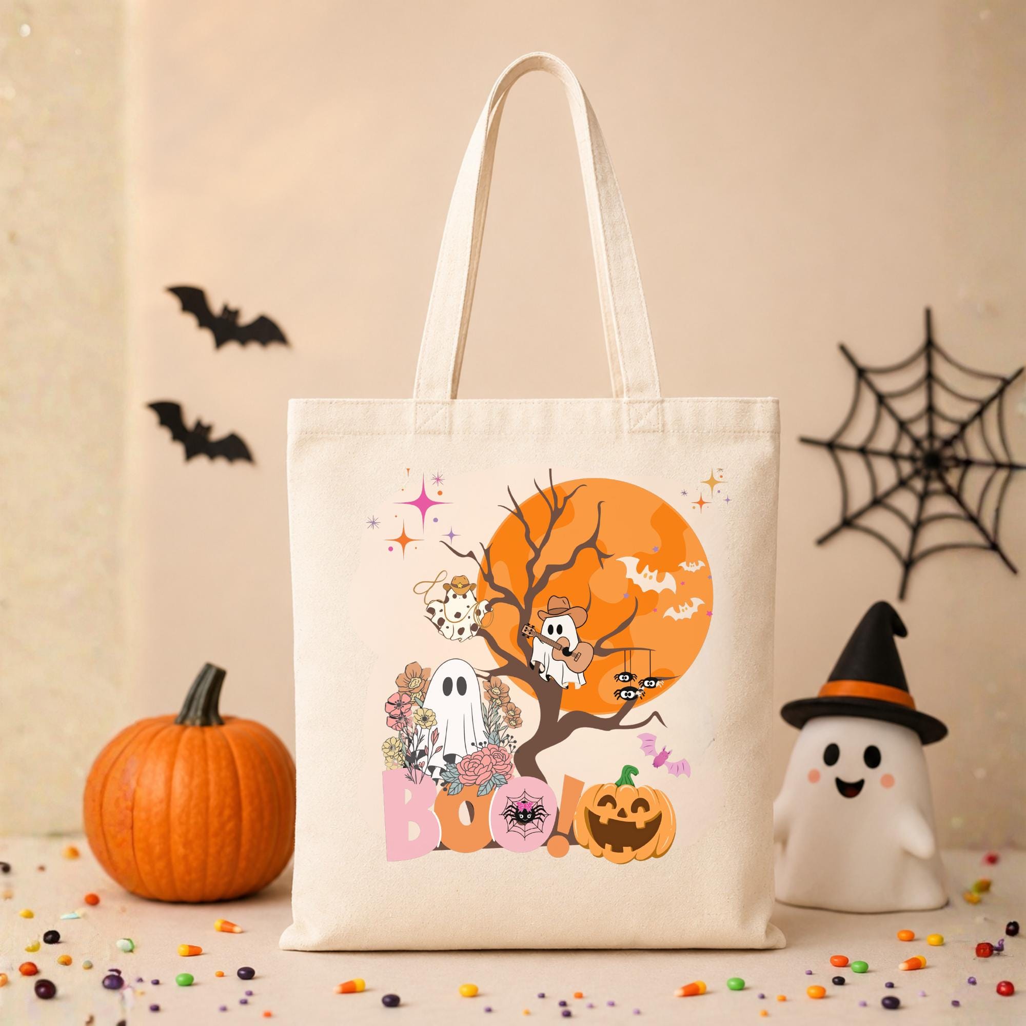 Tan tote bag with a Halloween design featuring a ghost, a pumpkin, and bats in front of a full moon. The text "BOO!" is printed on the bag.