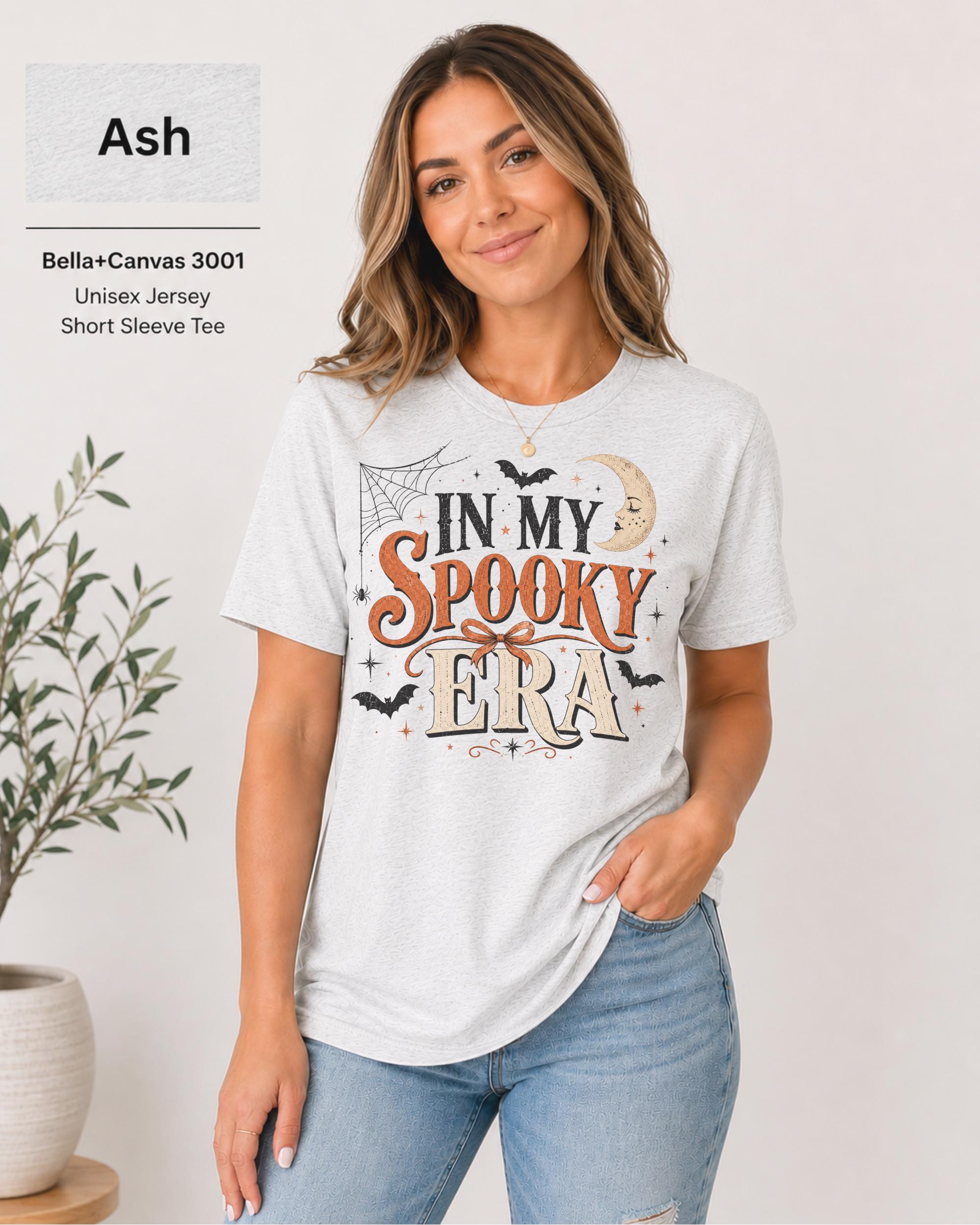 Bella+Canvas 3001 Ash unisex t-shirt featuring an "In My Spooky Era" Halloween graphic with vintage lettering, bats, crescent moon, spiderweb, and autumn-inspired artwork.
