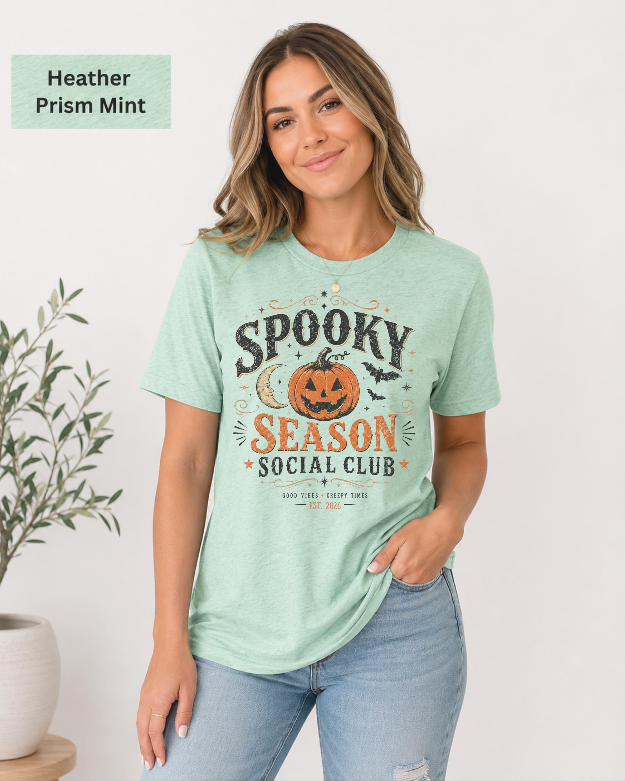 Bella+Canvas 3001 Heather Prism Mint unisex t-shirt featuring a vintage "Spooky Season Social Club" graphic with a smiling pumpkin, crescent moon, bats, and distressed autumn typography for Halloween and fall.